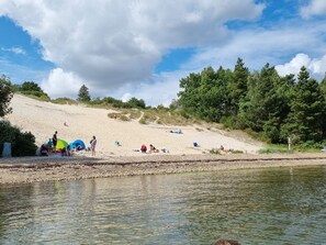 A beach with tents and people, a river, and trees.