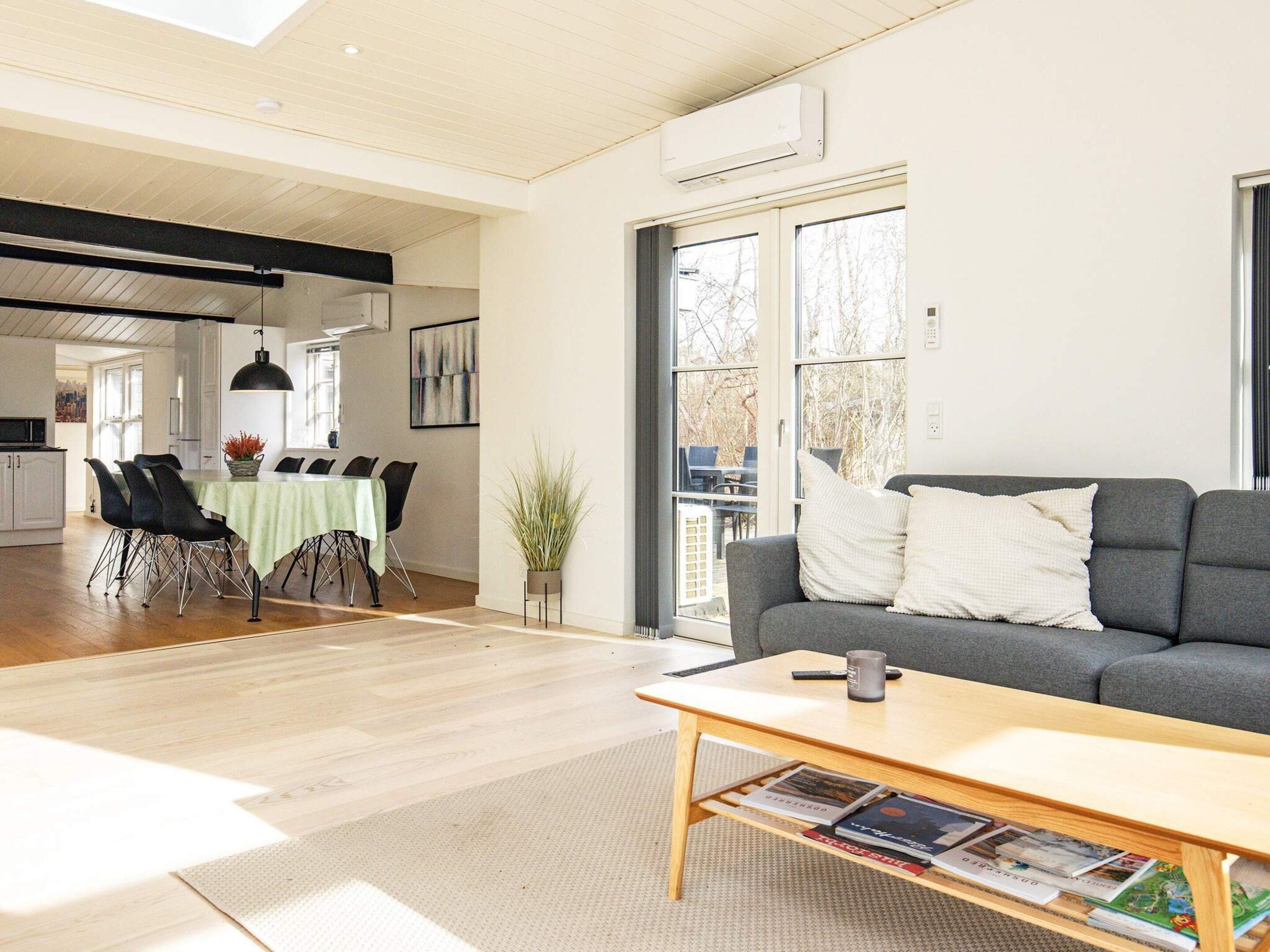 Ein modernes Wohnzimmer mit einem grauen Sofa, einem Holztisch und einem Essbereich mit einer grünen Tischdecke.