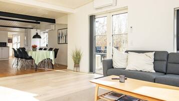 A modern living room with a grey sofa, a wooden coffee table, and a dining area with a green tablecloth.