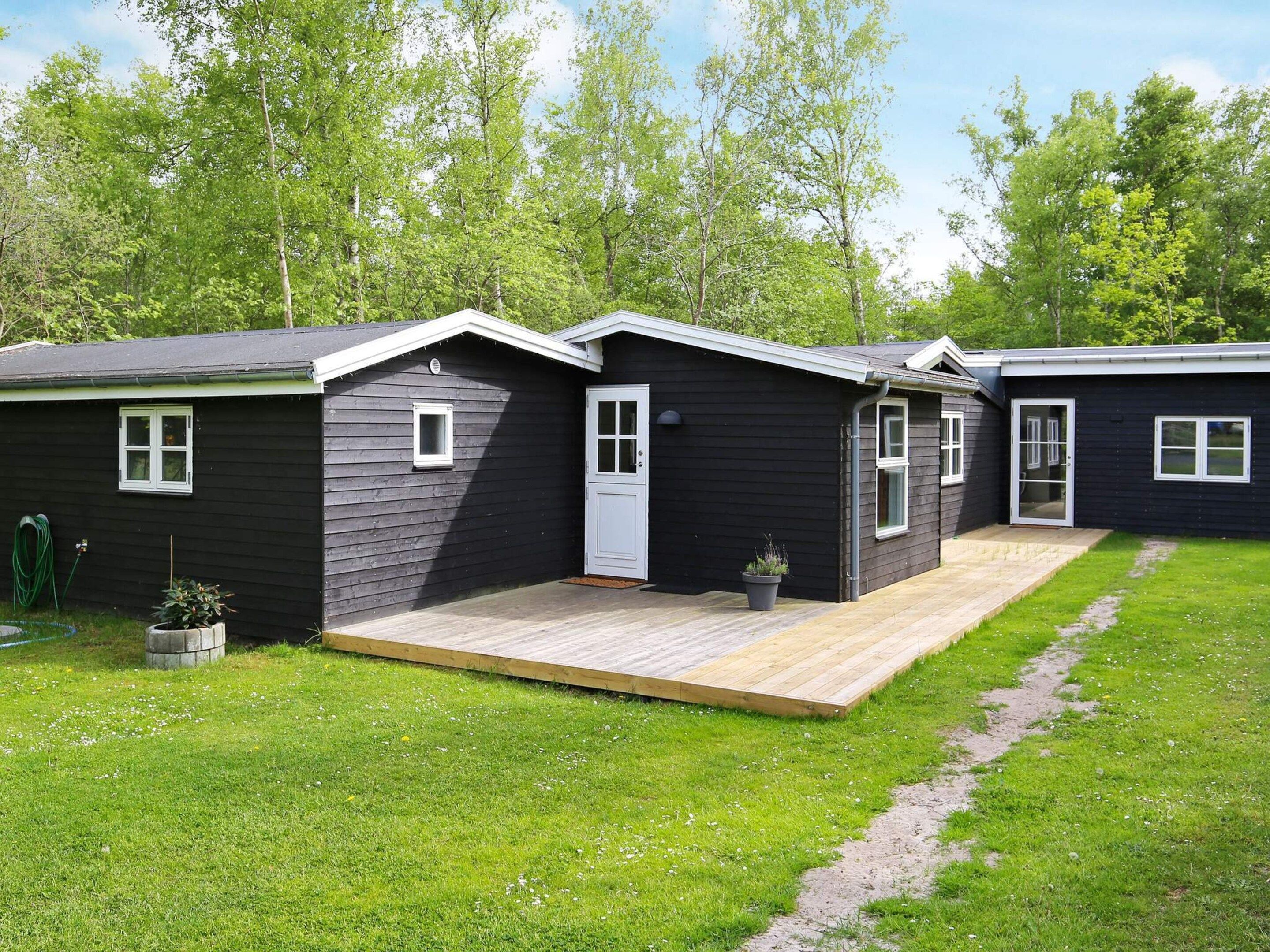 A row of dark-colored cabins with a wooden deck in front, surrounded by green grass and trees.