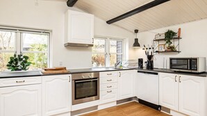 A kitchen with white cabinetry, a stainless steel oven, a microwave, and a window with a view of greenery.