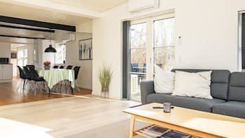 A modern living room with a grey sofa, a wooden coffee table, and a dining area with a green tablecloth.