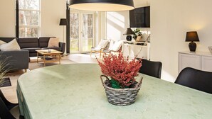 A modern living room with a dining table, a black pendant lamp, and a potted plant.