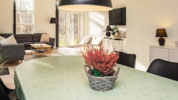 A modern living room with a dining table, a black pendant lamp, and a potted plant.