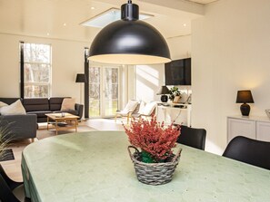 Ein modernes Wohnzimmer mit einem Esstisch, einer schwarzen Pendelleuchte und einem Blumentopf.