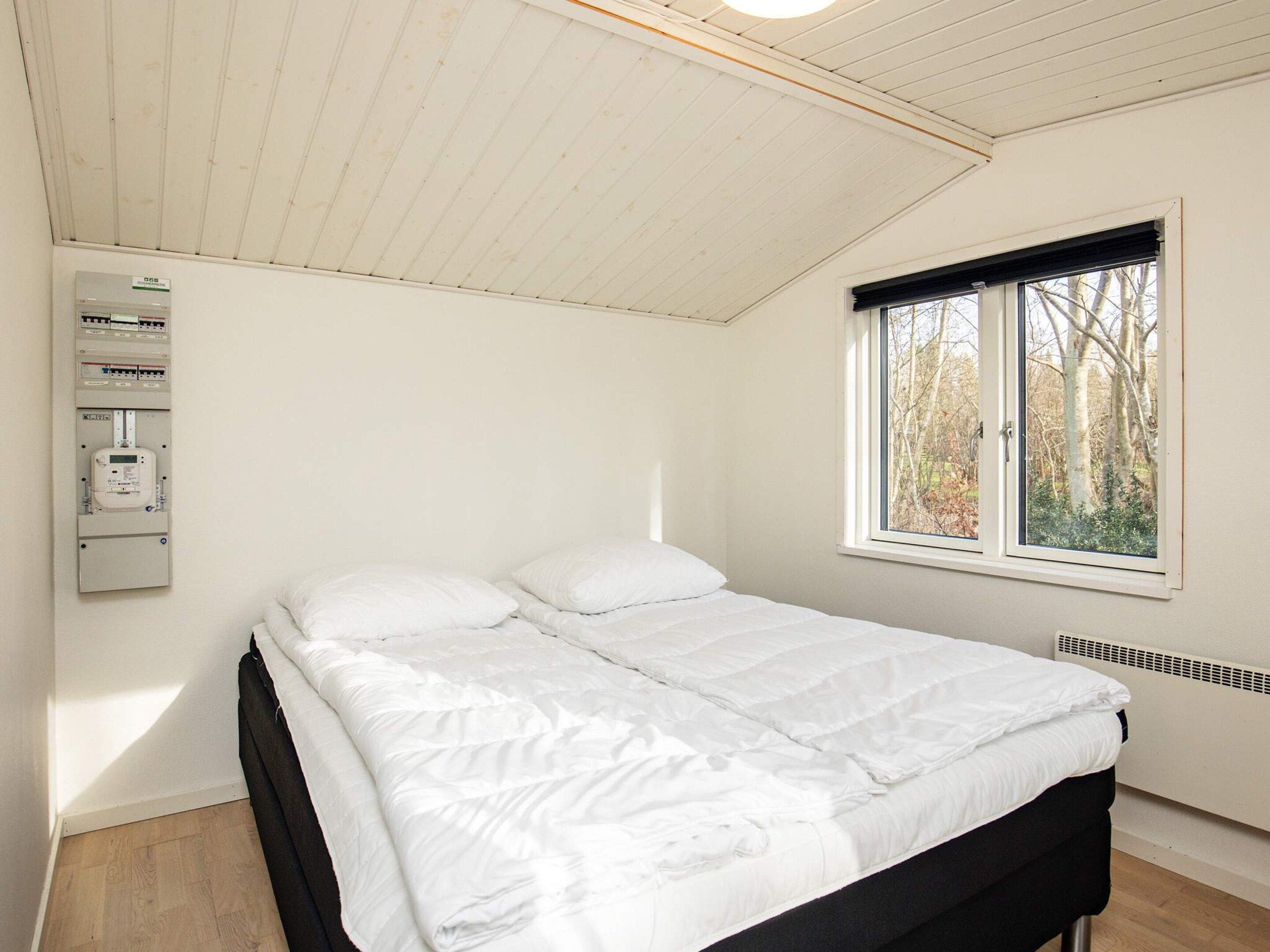 A bedroom with a bed, a window, and an electrical panel.