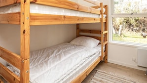 A bunk bed with a wooden frame, white bedding, and a window with a view of trees.