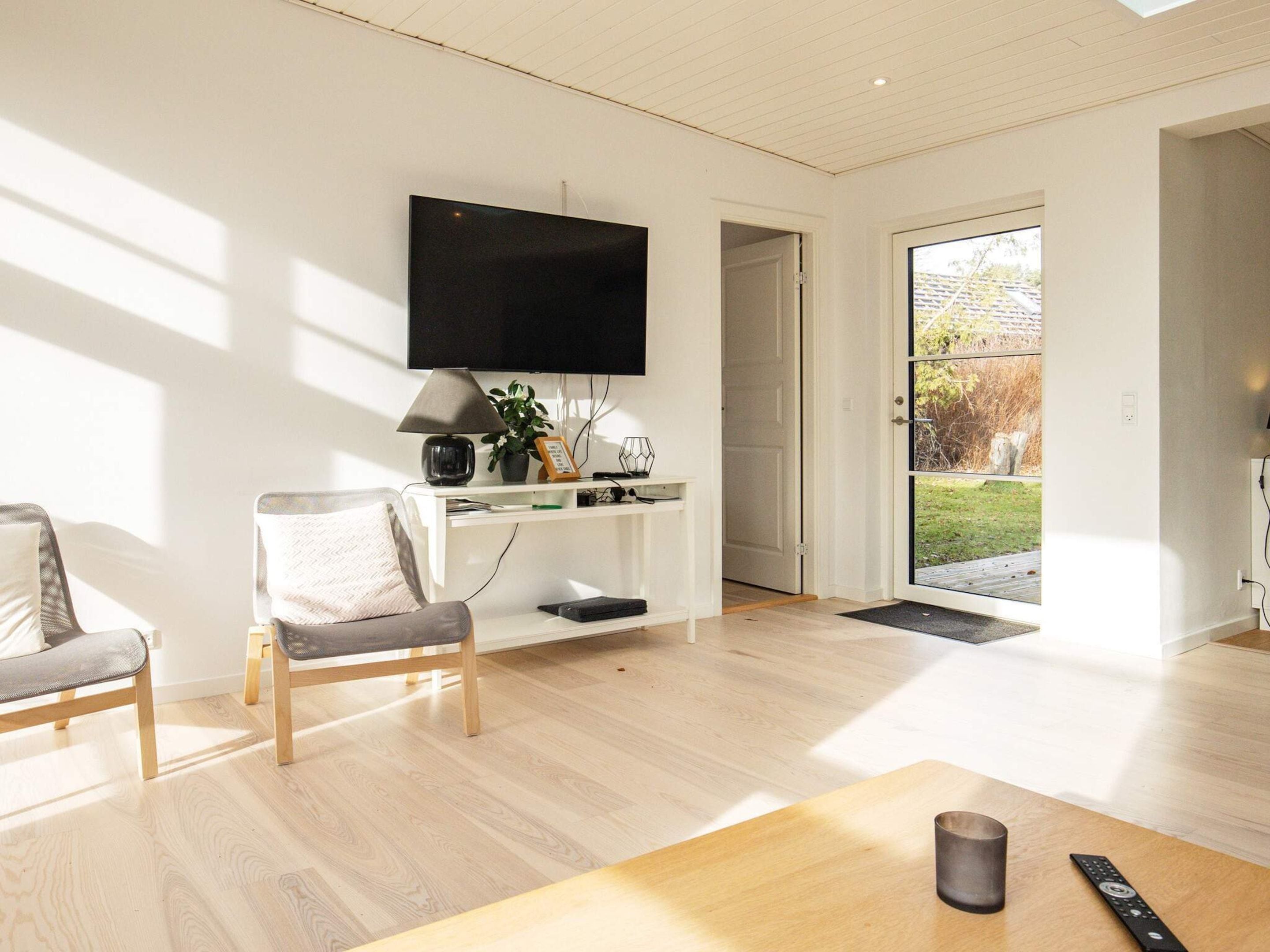 A modern living room with a flat-screen TV, a coffee table, a chair, and a door leading outside.