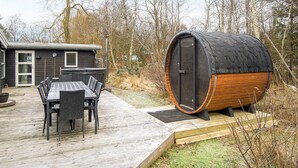 A wooden deck with a table and chairs, a sauna, and a house in the background. - 4 Star Holiday Home in Vig (Vig)