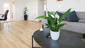 A living room with a sofa, a coffee table with a plant, a chair, and a remote control on the table. - 4 Person Holiday Home in Fjerritslev (Fjerritslev)