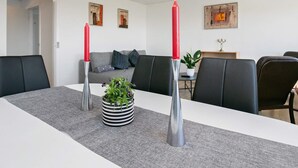 A modern dining room with a white table, grey rug, black chairs, a grey sofa, and a red candle in a silver holder. - 4 Person Holiday Home in Fjerritslev (Fjerritslev)
