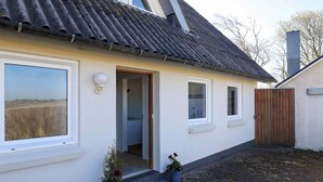 A single-story house with a tiled roof, a large window, and a door leading to a covered porch. There are two potted plants on the porch. - 4 Person Holiday Home in Fjerritslev (Fjerritslev)