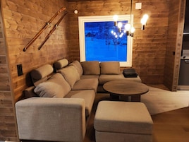 Una habitación acogedora con paredes de madera, un ventanal con vistas a un paisaje nevado, un sofá, una mesita pequeña y un esquí en la pared.