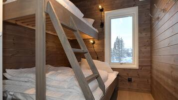 A wooden cabin room with a bunk bed, a window with a snowy view, and a wall-mounted light fixture.