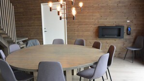 Une salle de conférence dotée d’une grande table ronde, de chaises grises à revêtement en tissu, d’un luminaire moderne et d’un téléviseur à écran plat fixé au mur.