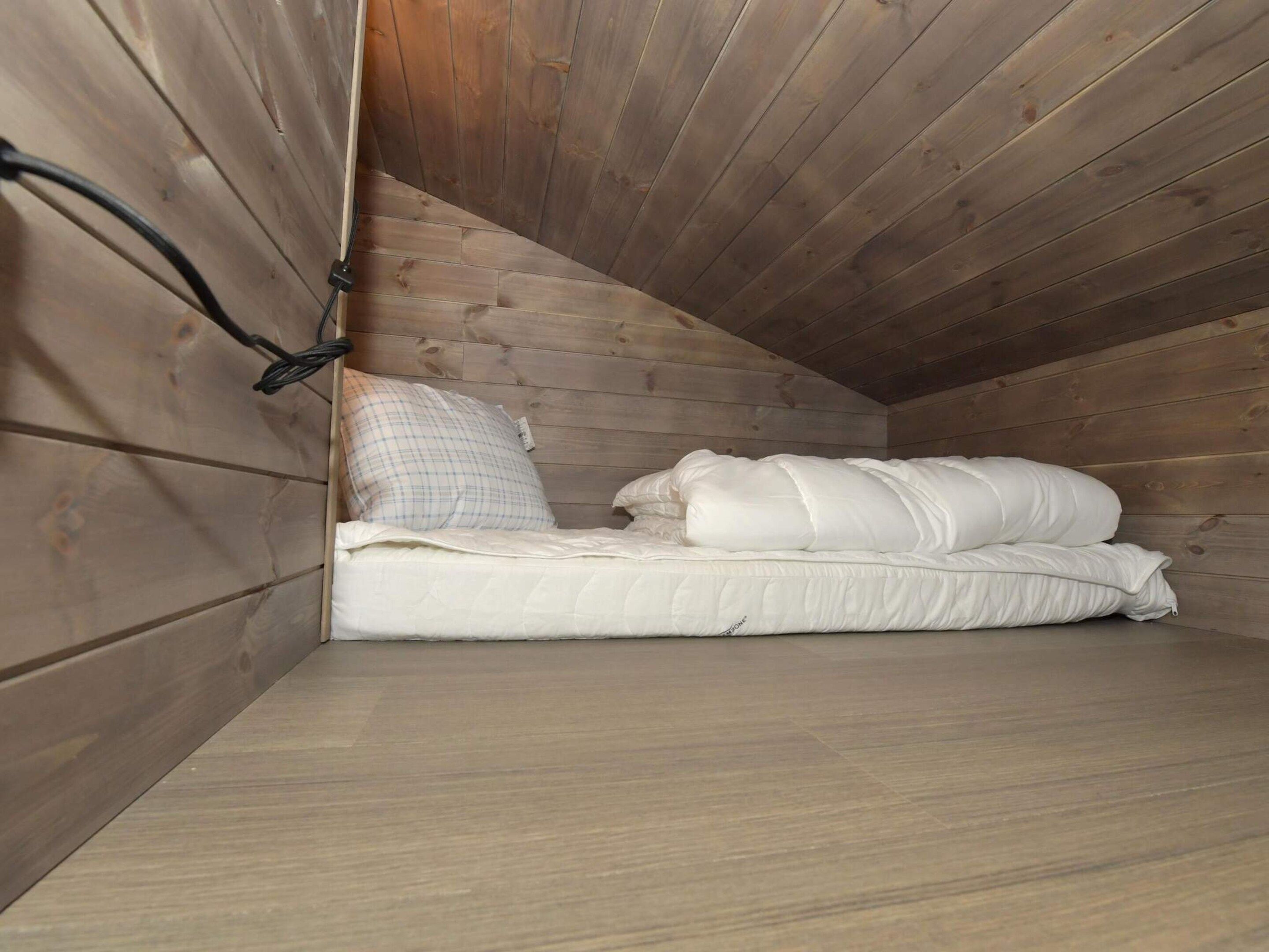 A small, sloped ceiling room with a bed, a pillow, and a power outlet on the wall.