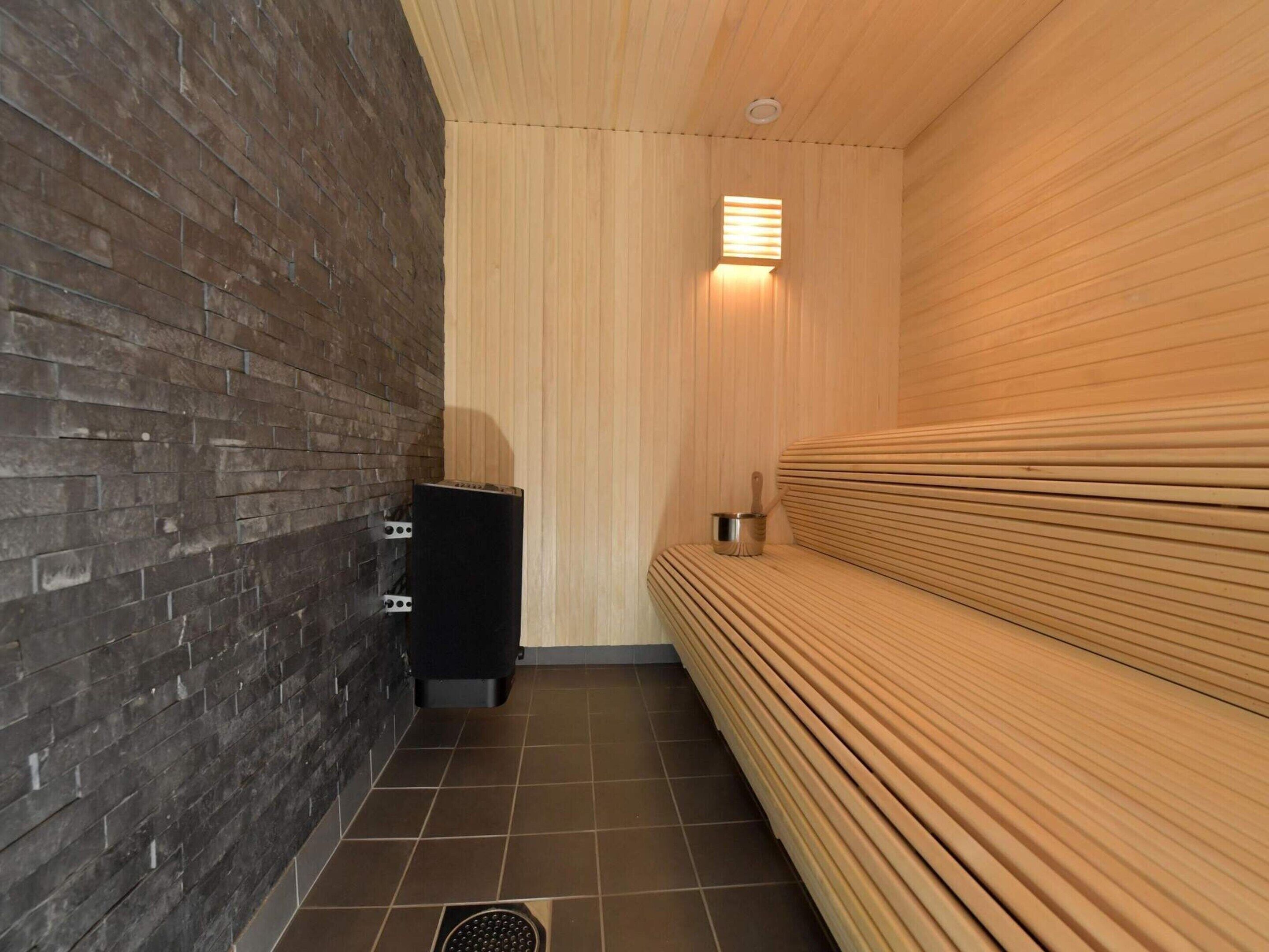 A sauna room with a wooden bench, a black heater, and a tiled floor.
