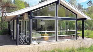 A modern glass house with a sloped roof, large windows, and a patio area with outdoor furniture. - 8 Person Holiday Home in Hadsund (Hadsund)