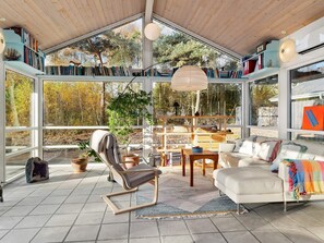 A spacious room with a high ceiling, large windows, and a wooden ceiling. There is a white sofa, a chair, and a small table with a bowl. Shelves with books and decorative items are visible. - 8 Person Holiday Home in Hadsund (Hadsund)