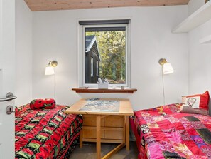 A small, cozy room with two beds, a wooden table, and a window with a view of a house and trees. - 8 Person Holiday Home in Hadsund (Hadsund)