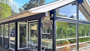 A modern glass house with a sloped roof, large windows, and a patio area with outdoor furniture. - 8 Person Holiday Home in Hadsund (Hadsund)