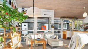 A modern living room with a sofa, coffee table, and a chair. There is a bookshelf, a dining area, and a kitchen visible. - 8 Person Holiday Home in Hadsund (Hadsund)