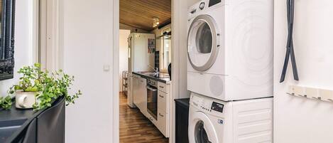 A laundry area with stacked washing machines, a fire extinguisher, and a potted plant.