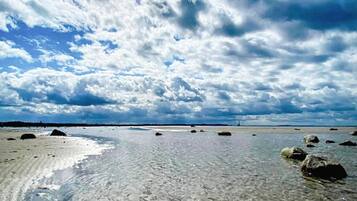 En strand med klart vatten, klippor och en molnig himmel.