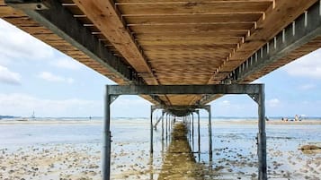 A wooden pier structure with a metal framework extending into a beach area.