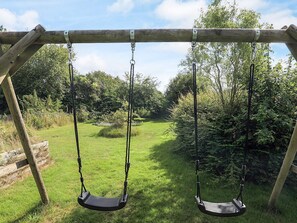 A wooden swing set in a grassy area with trees in the background.