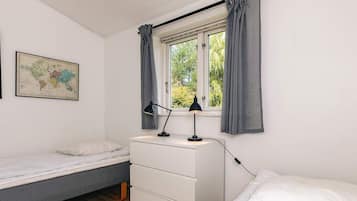A bedroom with a bed, a desk with a lamp, a dresser, a window with curtains, and a world map on the wall.