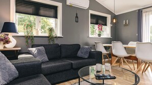 A modern living room with a grey sofa, a glass coffee table, and a dining area with a wooden table and white chairs. - 4 Star Holiday Home in Jaegerspris (Jægerspris)