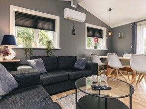 A modern living room with a grey sofa, a glass coffee table, and a dining area with a wooden table and white chairs.