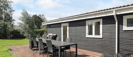 A wooden deck with a dining table and chairs, a barbecue grill, and a small shed.