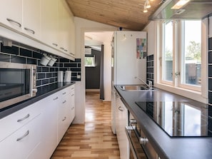 A modern kitchen with a microwave, oven, and stainless steel sink. - 4 Star Holiday Home in Jaegerspris (Jægerspris)