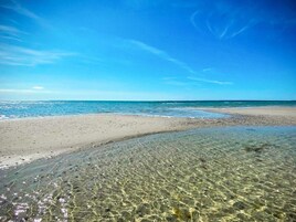 Una playa con aguas poco profundas y cristalinas, una orilla arenosa y un cielo azul despejado.