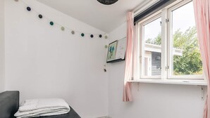 A small, neatly arranged bedroom with a single bed, a window with curtains, and a wall-mounted shelf with a framed picture. - 4 Star Holiday Home in Jaegerspris (Jægerspris)