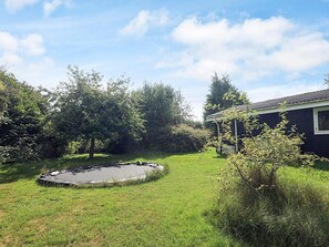 A backyard with a trampoline, a house, and surrounding greenery.