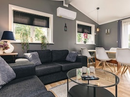 A modern living room with a grey sofa, a glass coffee table, and a dining area with white chairs.