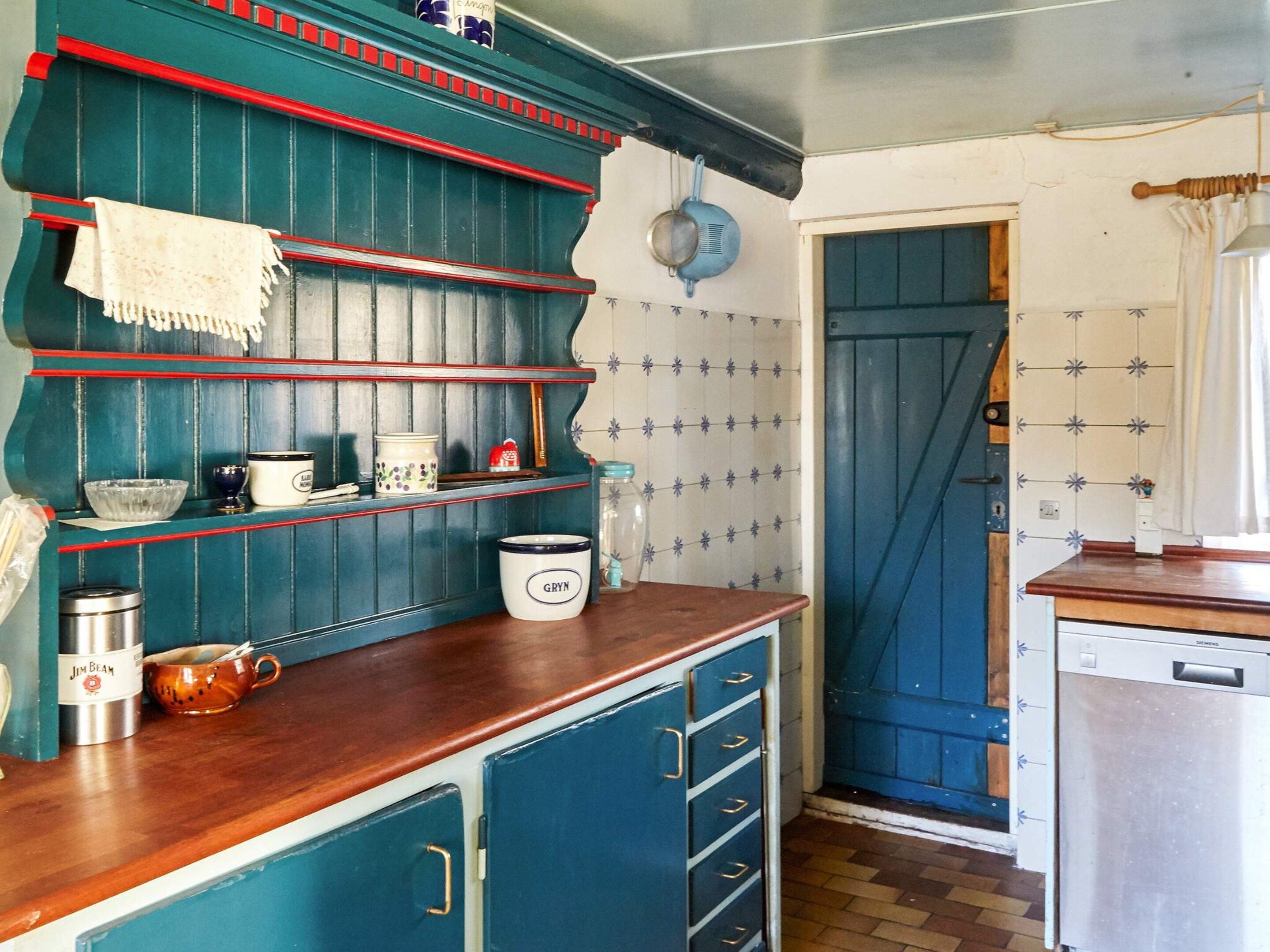 A kitchen with blue cabinets, a wooden countertop, and a blue door.