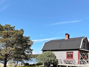 A house with a dark roof, white walls, and red trim. It is situated near a body of water with trees around. - 4 Star Holiday Home in Uddevalla (Uddevalla)