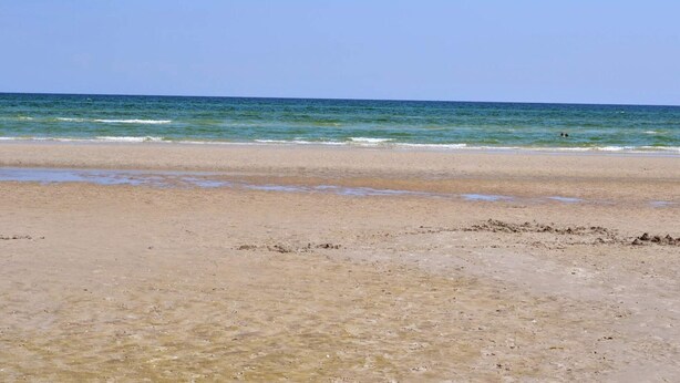 A beach with clear water, a sandy shore, and a person swimming in the distance.
