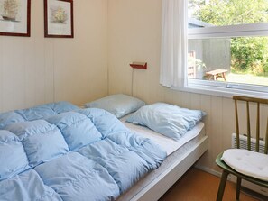 Ein Zimmer mit einem Einzelbett, einem Fenster, einem Sessel und zwei Bildern an der Wand.