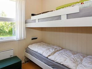 Een stapelbed met een onderbed en een plank erboven. Er is een raam met gordijnen, een radiator en een groene bank.
