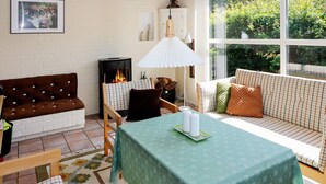 A cozy room with a fireplace, a dining table with candles, a sofa, and a large window with a view of greenery.