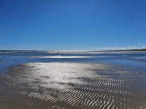 Een strand met natte zandpatronen en een helderblauwe lucht.