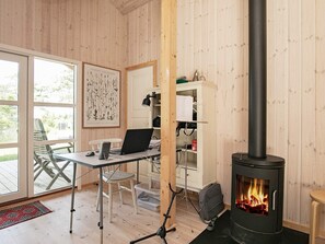 A cozy room with a wooden interior, a desk with a laptop, a chair, a bookshelf, and a wood-burning stove.