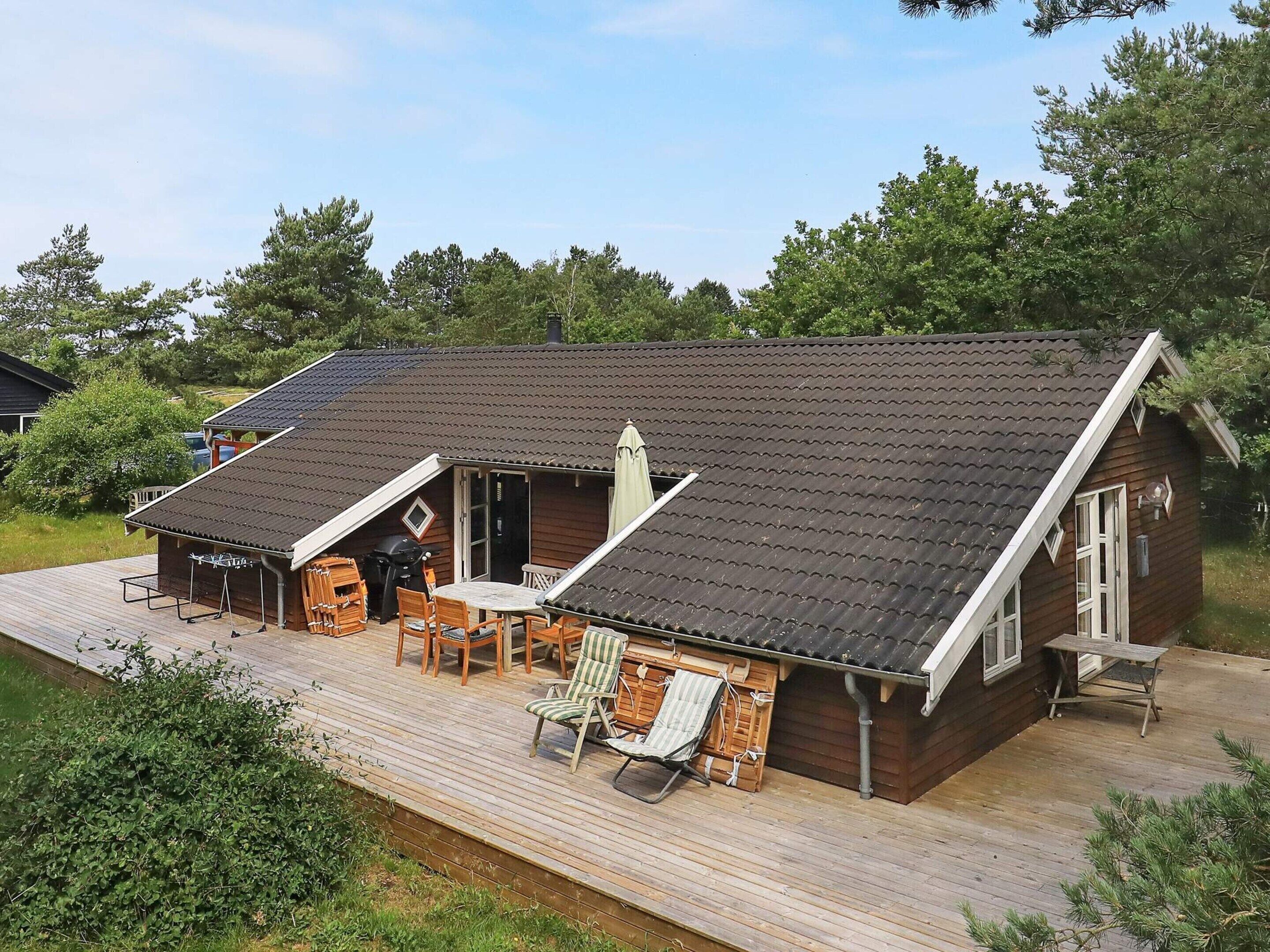 A wooden cabin with a sloped roof, a deck with outdoor furniture, and a small attached garage.