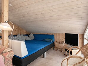 A loft-style bedroom with a sloped ceiling, a bed with blue bedding, a television, and a wicker chair.