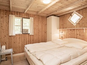 A wooden-paneled room with a bed, a window with curtains, a bedside table, and a wall-mounted light fixture. - 12 Person Holiday Home in Laeso (Læsø)